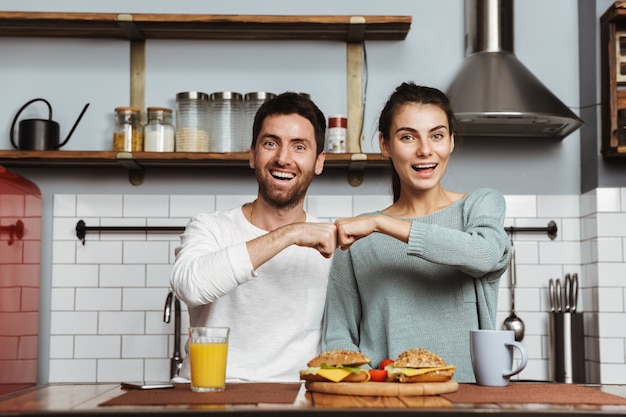 Jovem casal feliz sentado na cozinha durante o café da manhã em casa, batendo o punho