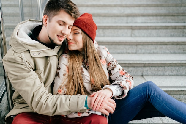 Jovem casal feliz sorrindo com os olhos fechados e sentado na escada.