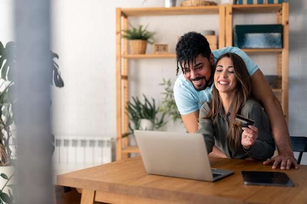 Jovem casal feliz usando laptop e cartão de crédito enquanto faz compras na internet em casa