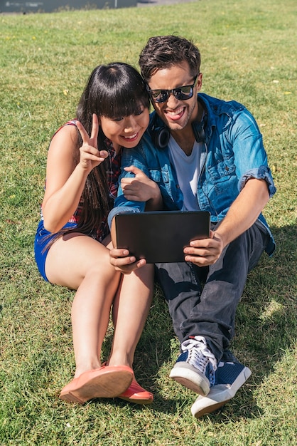 Jovem casal feliz usando tablet sentado no parque
