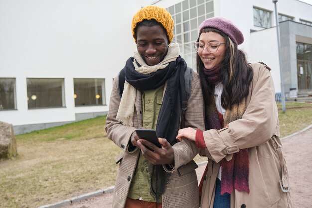 Jovem casal feliz vendo fotos no celular e rindo enquanto caminha ao ar livre