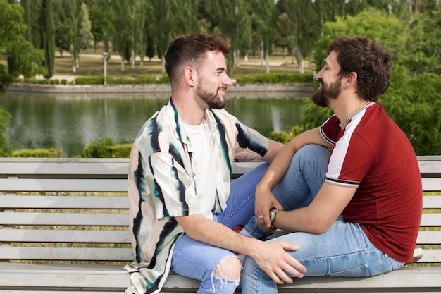 Jovem casal gay masculino olhando um ao outro enquanto está sentado no parque