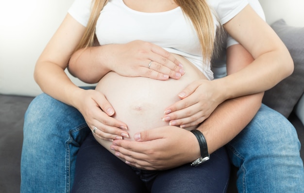 Jovem casal grávida de mãos dadas na barriga grande