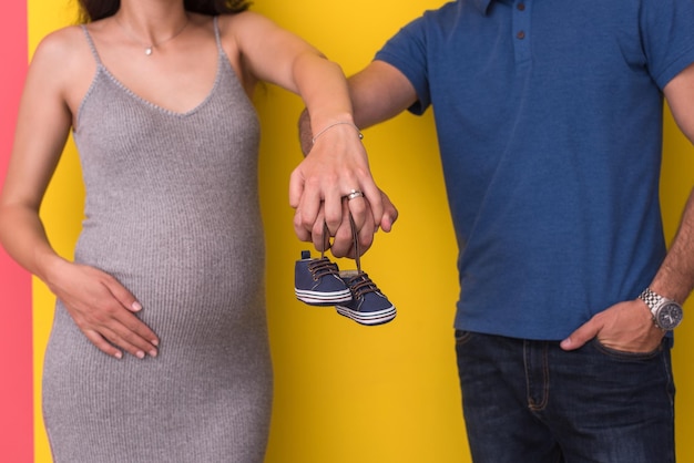 jovem casal grávida segurando sapatos de bebê recém-nascido isolado em fundo amarelo,conceito de família e paternidade