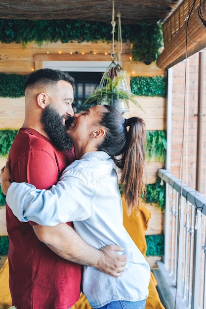 Jovem casal heterossexual no terraço de uma casa abraçando e sorrindo um para o outro