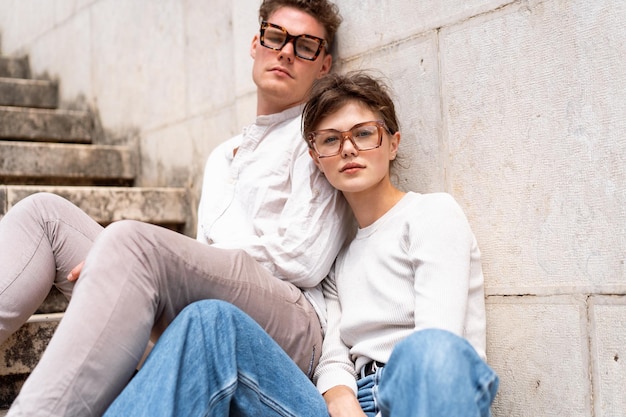 Jovem casal hipster lindo em óculos de sol apaixonados sentado escadas na rua da cidade velha