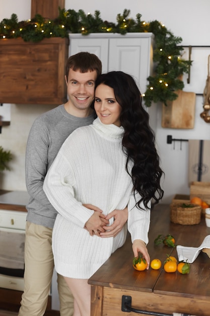 Jovem casal homem bonito e linda garota modelo posando na cozinha decorada na manhã de Natal