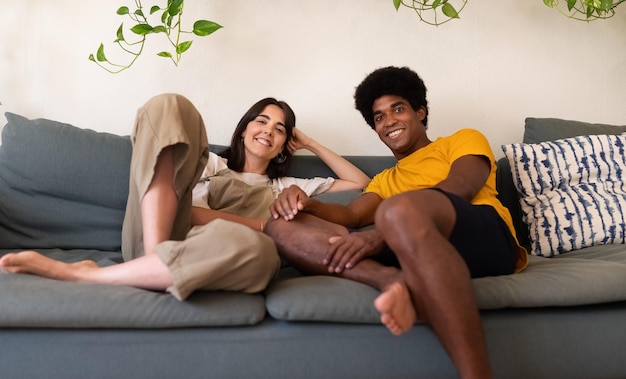 Jovem casal interracial relaxando sentado no sofá olhando para a câmera