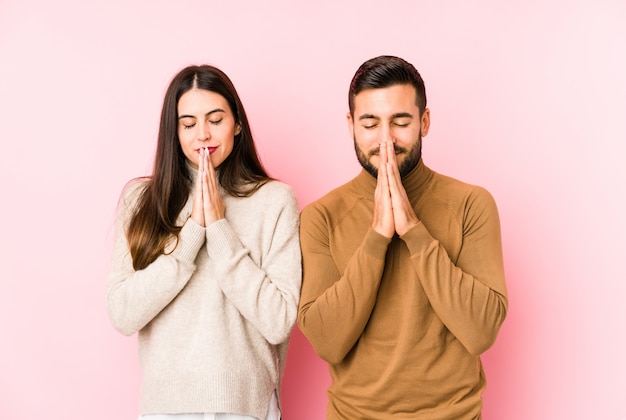 Jovem casal isolado de mãos dadas em orar perto da boca, sente-se confiante