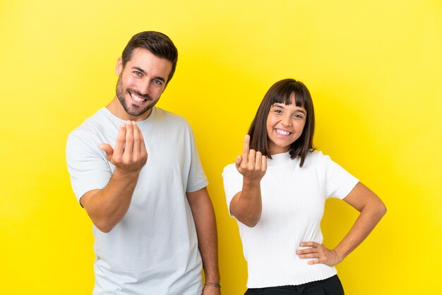 Foto jovem casal isolado em fundo amarelo convidando para vir com a mão feliz por você ter vindo