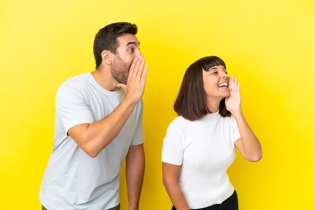 Jovem casal isolado em fundo amarelo gritando com a boca aberta para o lado