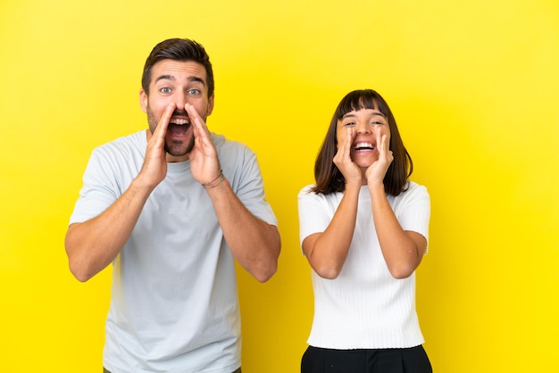 Jovem casal isolado em fundo amarelo gritando e anunciando algo