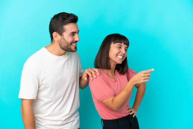 Jovem casal isolado em um fundo azul apontando para o lado para apresentar um produto