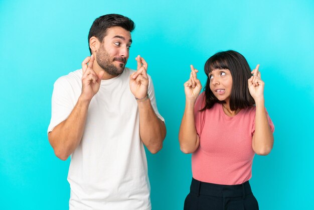 Jovem casal isolado em um fundo azul com os dedos se cruzando e desejando o melhor