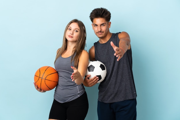 Jovem casal jogando futebol e basquete no azul apertando as mãos para fechar um bom negócio