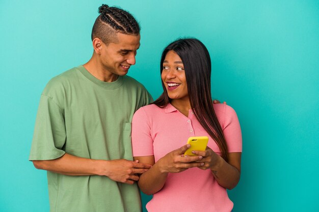 Jovem casal latino com um celular isolado em um fundo azul