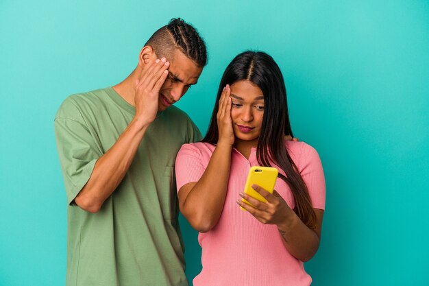 Jovem casal latino com um celular isolado em um fundo azul