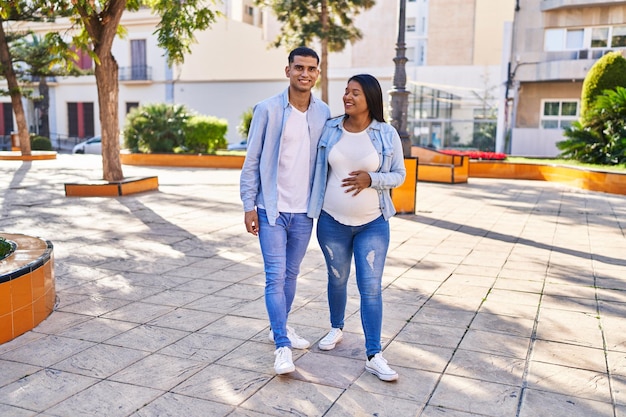 Jovem casal latino esperando bebê se abraçando andando no parque