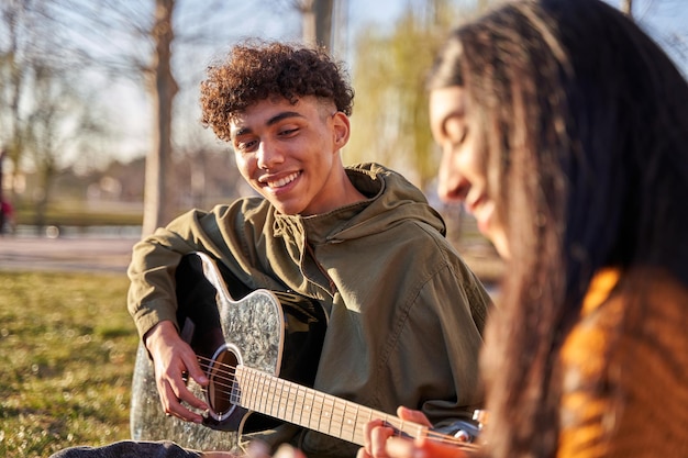 Jovem casal latino sentado na árvore tocando ukulele e violão cantando uma música sentindo-se feliz conceito relaxante