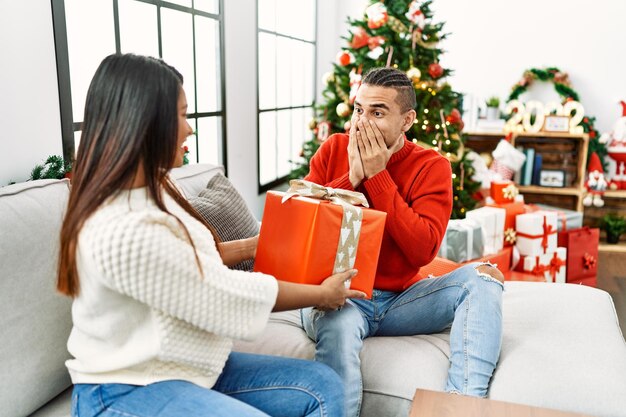 Jovem casal latino sorrindo feliz segurando o presente de natal em casa