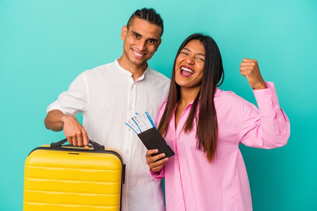 Jovem casal latino vai viajar isolado sobre fundo azul, levantando o punho após uma vitória, o conceito de vencedor.