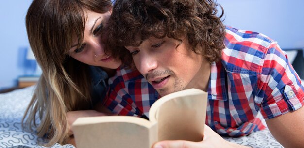 Jovem casal lendo um livro juntos, deitado na cama