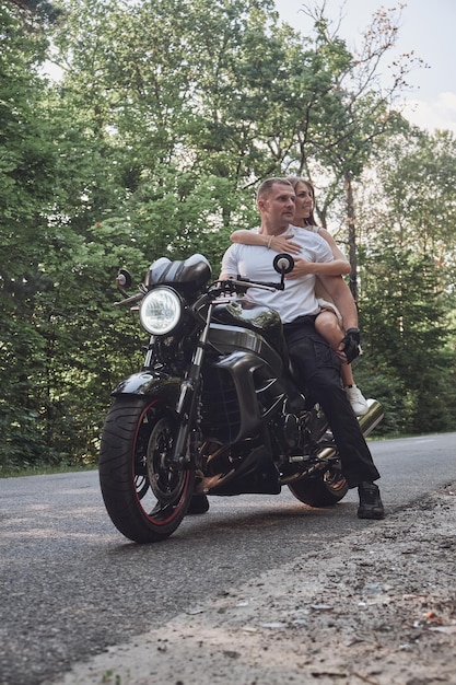 Jovem casal lindo abraçando sentado em uma motocicleta viajam juntos em uma estrada florestal