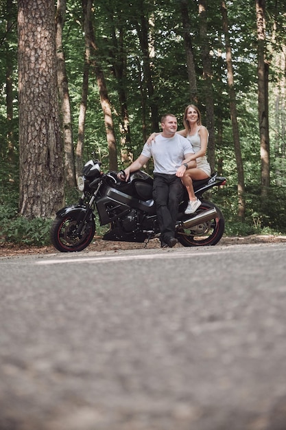 Jovem casal lindo abraçando sentado em uma motocicleta viajam juntos em uma estrada florestal