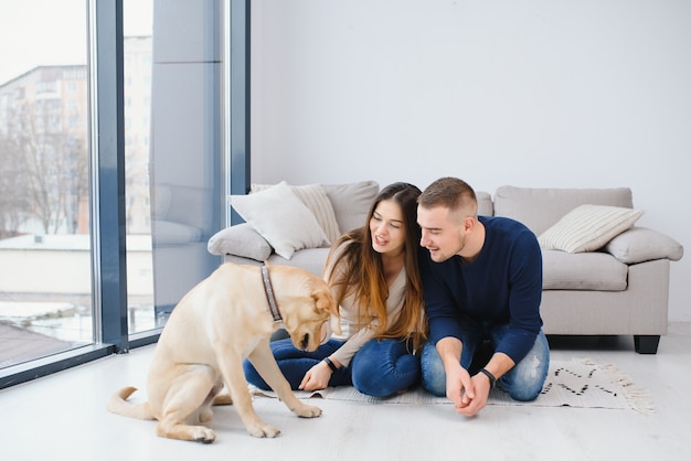 Jovem casal lindo com cachorro sentado no chão na nova casa
