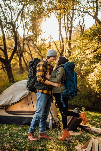 Jovem casal lindo com mochila de caminhada se beijando na floresta perto da barraca