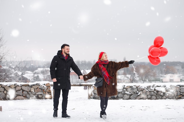 Jovem casal lindo com roballs vermelhos ao ar livre em tempo de neve