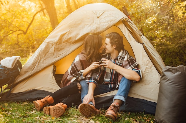 Jovem casal lindo em vestido casual sentado em um acampamento perto da tenda