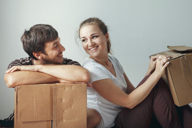 Jovem casal lindo recém-casado sentado no chão de um apartamento novo, após o reparo entre as caixas de papelão, está feliz e sorrindo.