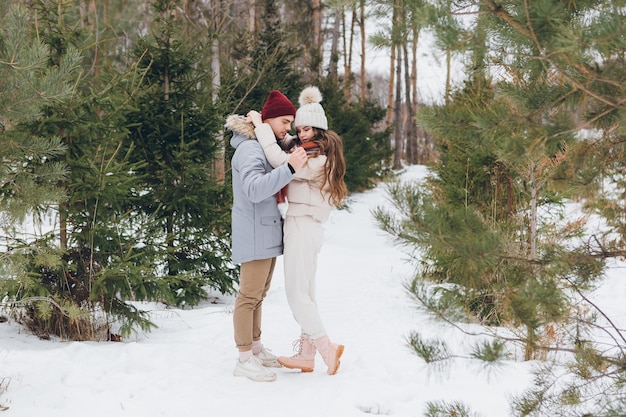 Jovem casal lindo se abraçando em uma floresta de coníferas de inverno