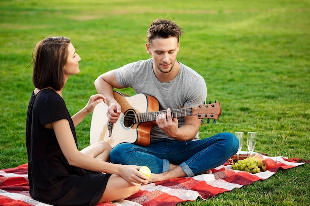 Jovem casal lindo sorrindo descansando no piquenique no parque