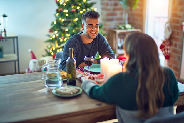 Jovem casal lindo sorrindo feliz e confiante. Comendo comida comemorando o natal em casa