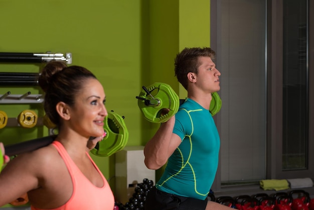 Jovem casal malhando pernas com barra no agachamento de centro de fitness