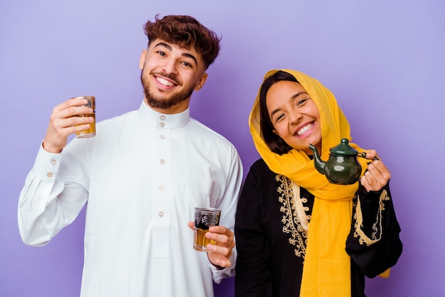 Jovem casal marroquino bebendo chá comemorando o mês do ramadã isolado em fundo roxo