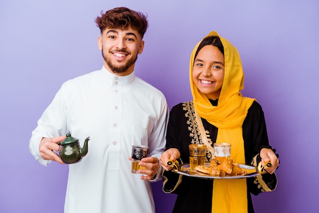 Jovem casal marroquino bebendo chá comemorando o mês do ramadã isolado na parede roxa