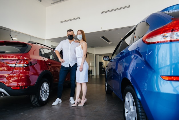 Jovem casal mascarado escolhe um novo veículo e consulta um representante da concessionária no período da pandemia. Venda de carros e vida durante a pandemia.