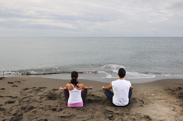 Jovem casal meditando ioga em posição de lótus no início da manhã na praia