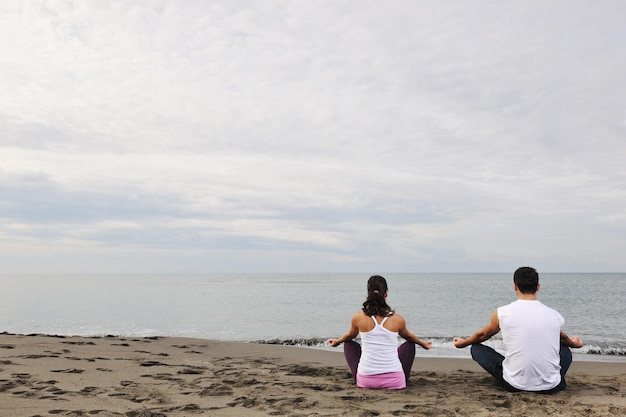 jovem casal meditando ioga em posição de lótus no início da manhã na praia