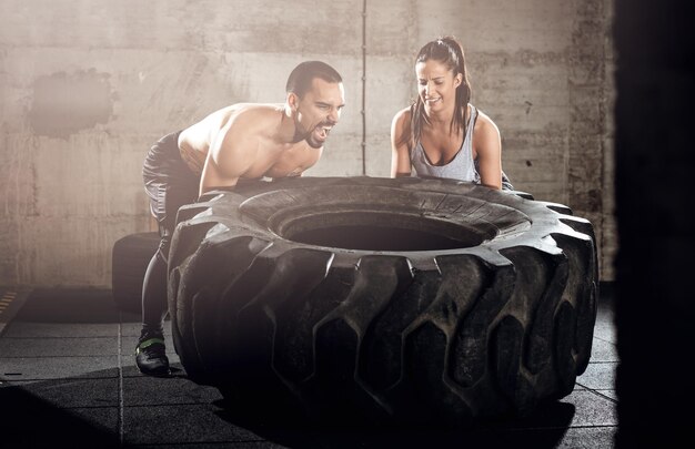 Jovem casal musculoso lançando um pneu no treinamento cross fit no ginásio.