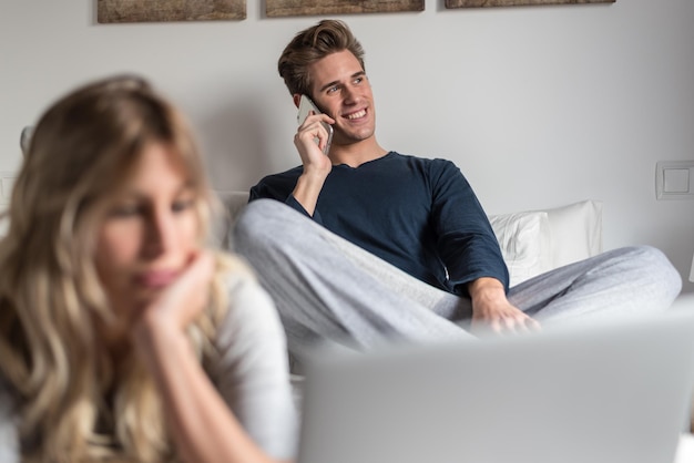 Foto jovem casal na cama entretido em seu computador e telefone