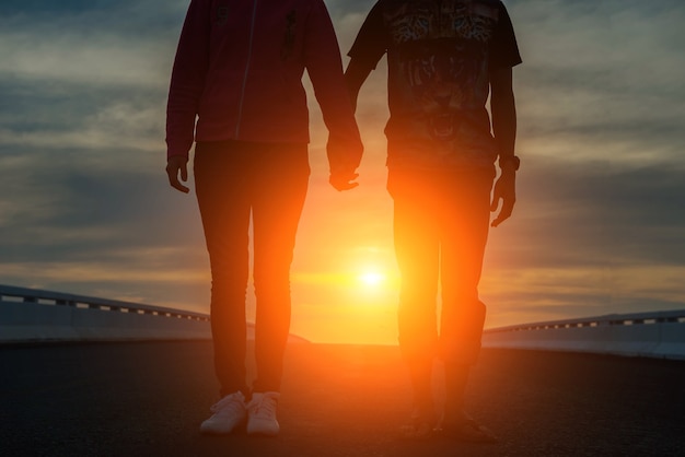 Foto jovem casal na estrada ao pôr do sol de mãos dadas.
