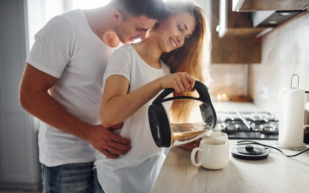 Jovem casal na manhã juntos em pé na cozinha moderna.