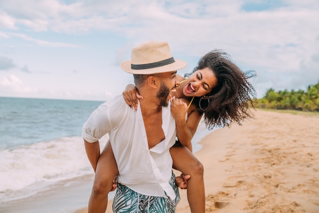 Jovem casal na praia, férias de verão, feliz e sorridente homem carregando uma mulher de volta à beira-mar