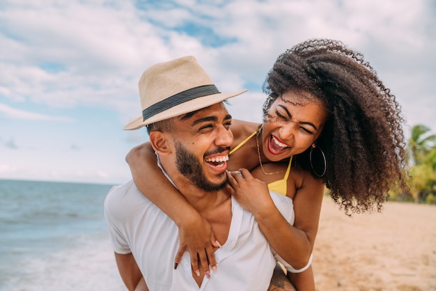 Jovem casal na praia, férias de verão, feliz e sorridente homem carregando uma mulher de volta à beira-mar