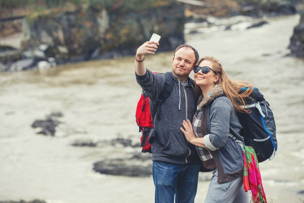 Jovem casal nas montanhas com mochilas na primavera fazendo uma selfie