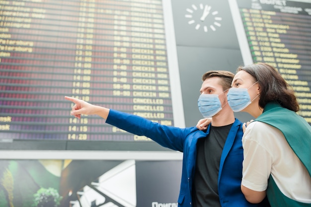 Jovem casal no aeroporto internacional, olhando para o quadro de informações de voo